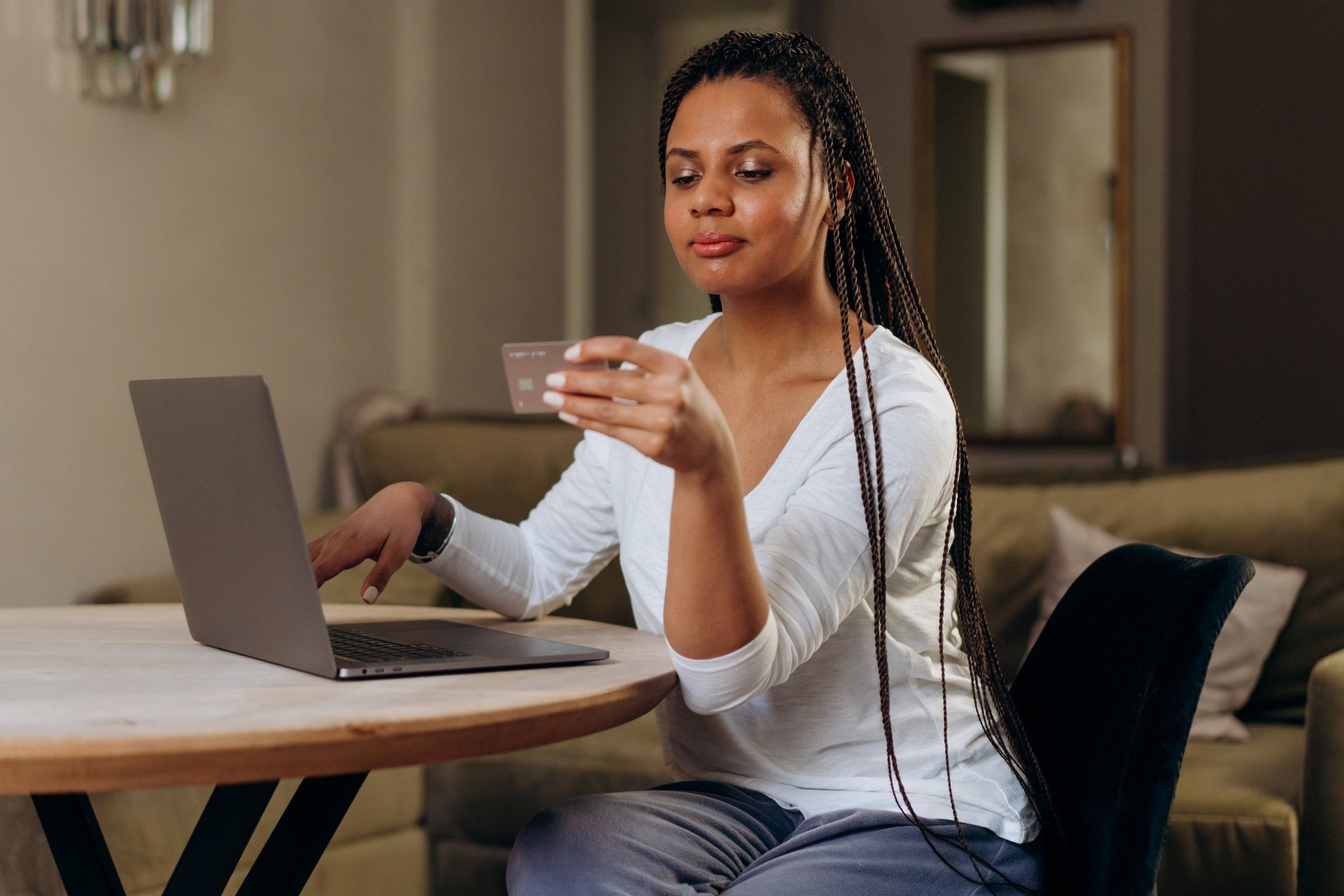 A woman is sitting at a table using a laptop and holding a credit card.