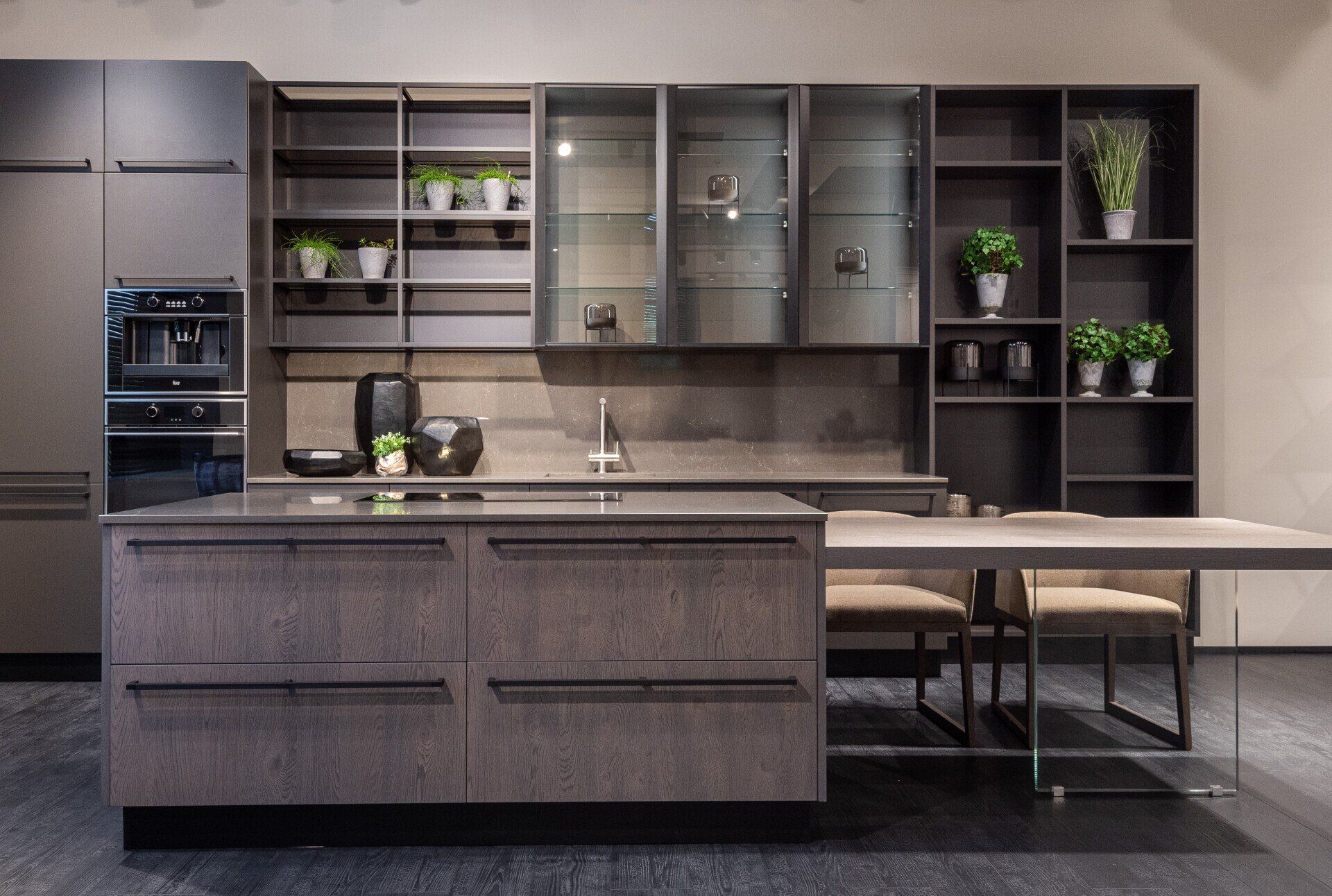 Modern kitchen with gray cabinetry, island, and dining table; shelves with plants.