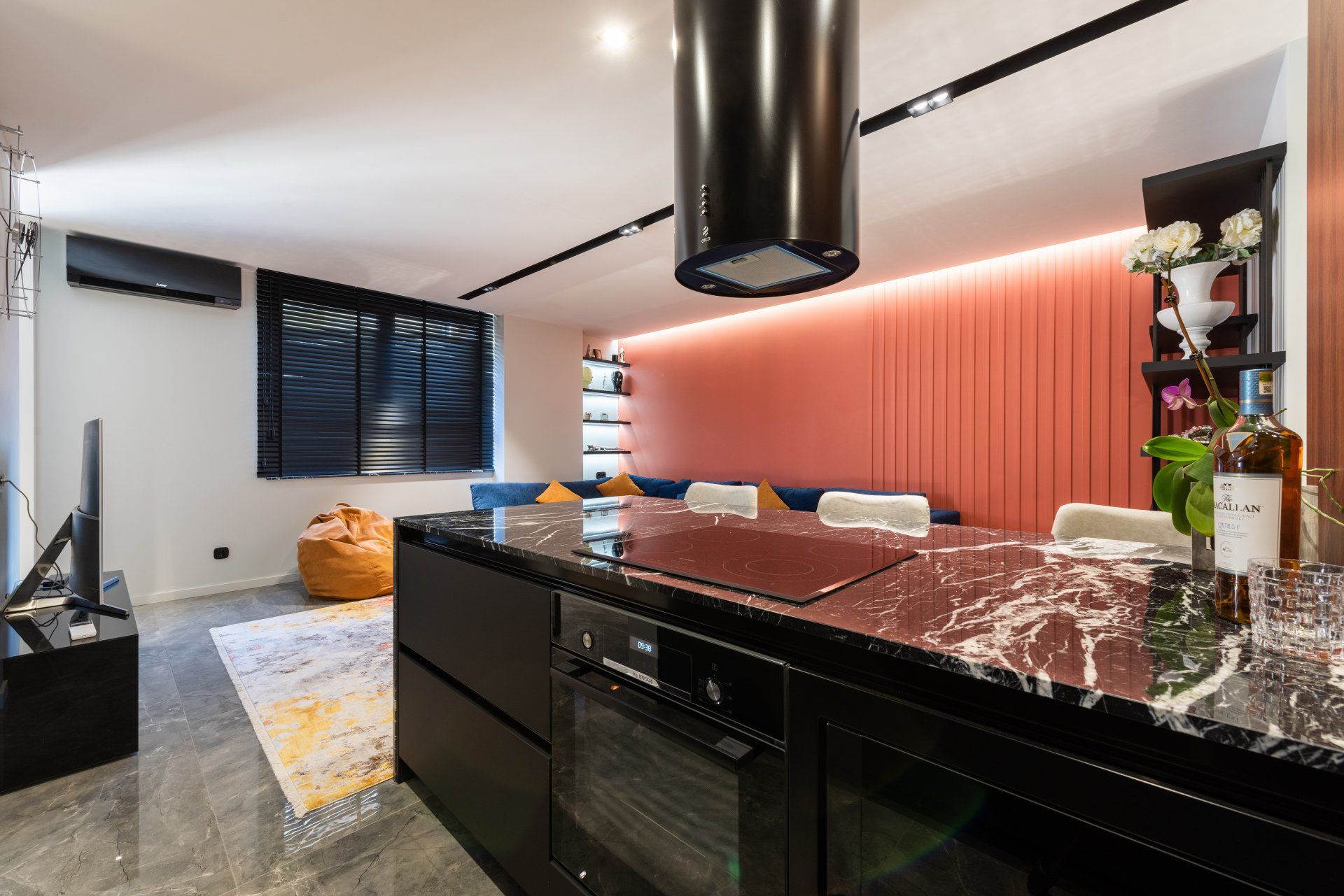 Modern kitchen with black island, marble countertop, and pink accent wall.