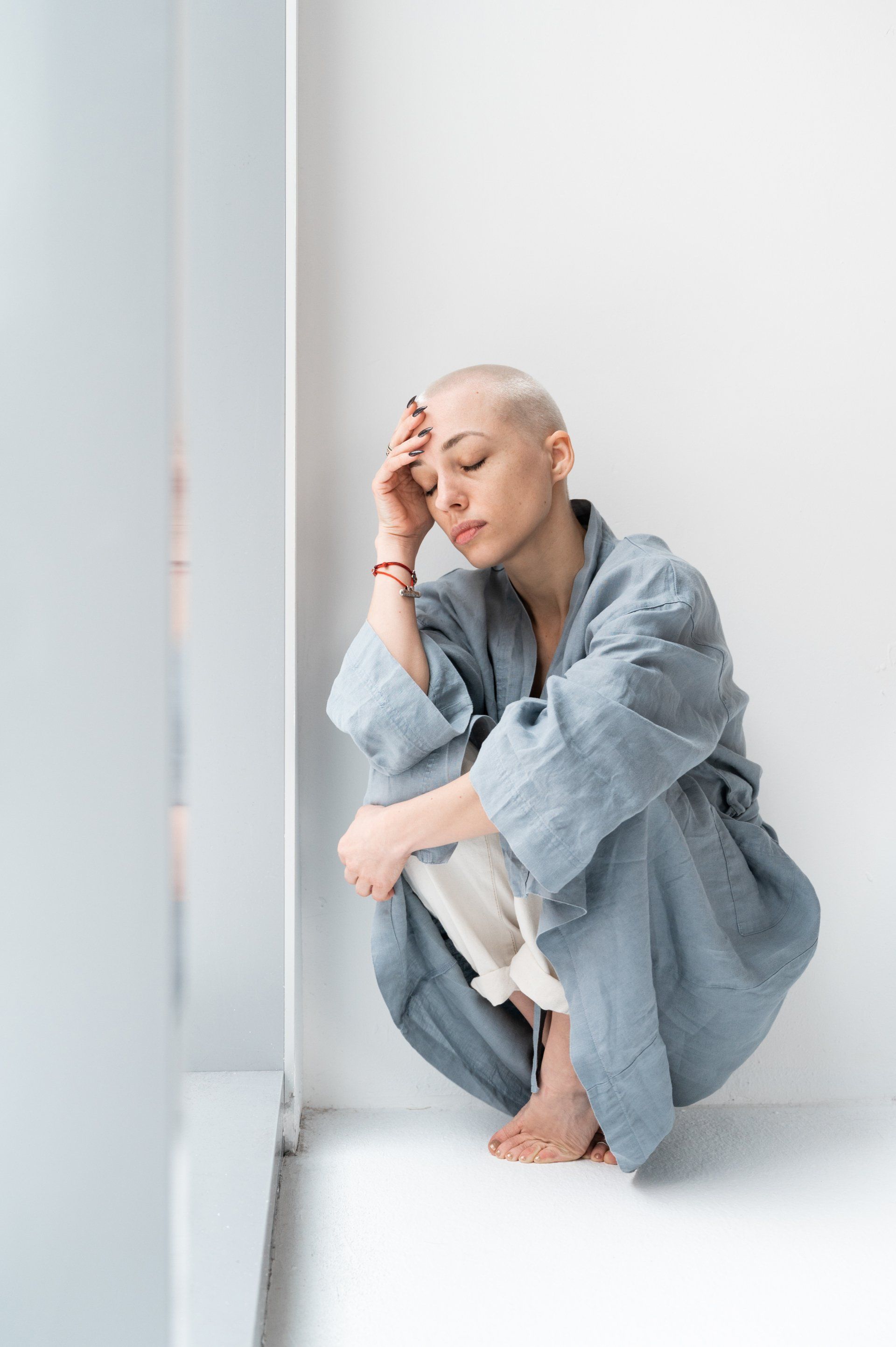 A bald woman is sitting on the floor in front of a window.
