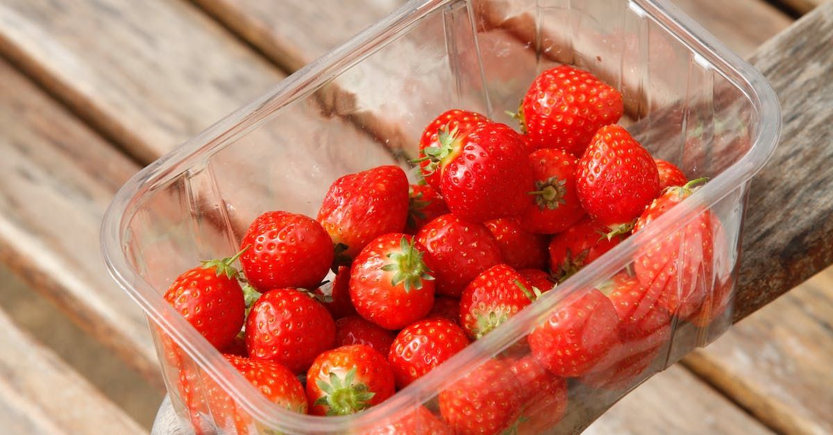 A plastic container filled with strawberries is sitting on a wooden table.