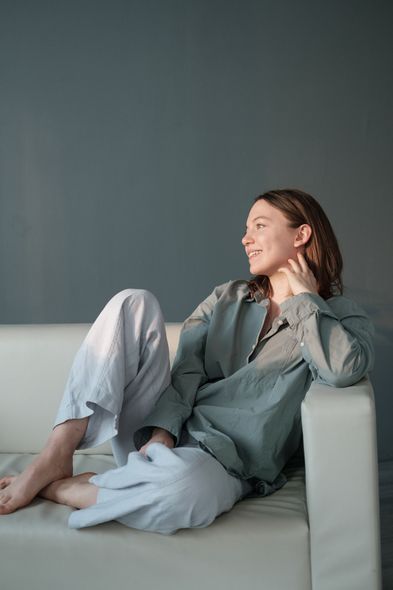 Woman reclining on a sofa, smiling in a gray outfit against a dark wall.