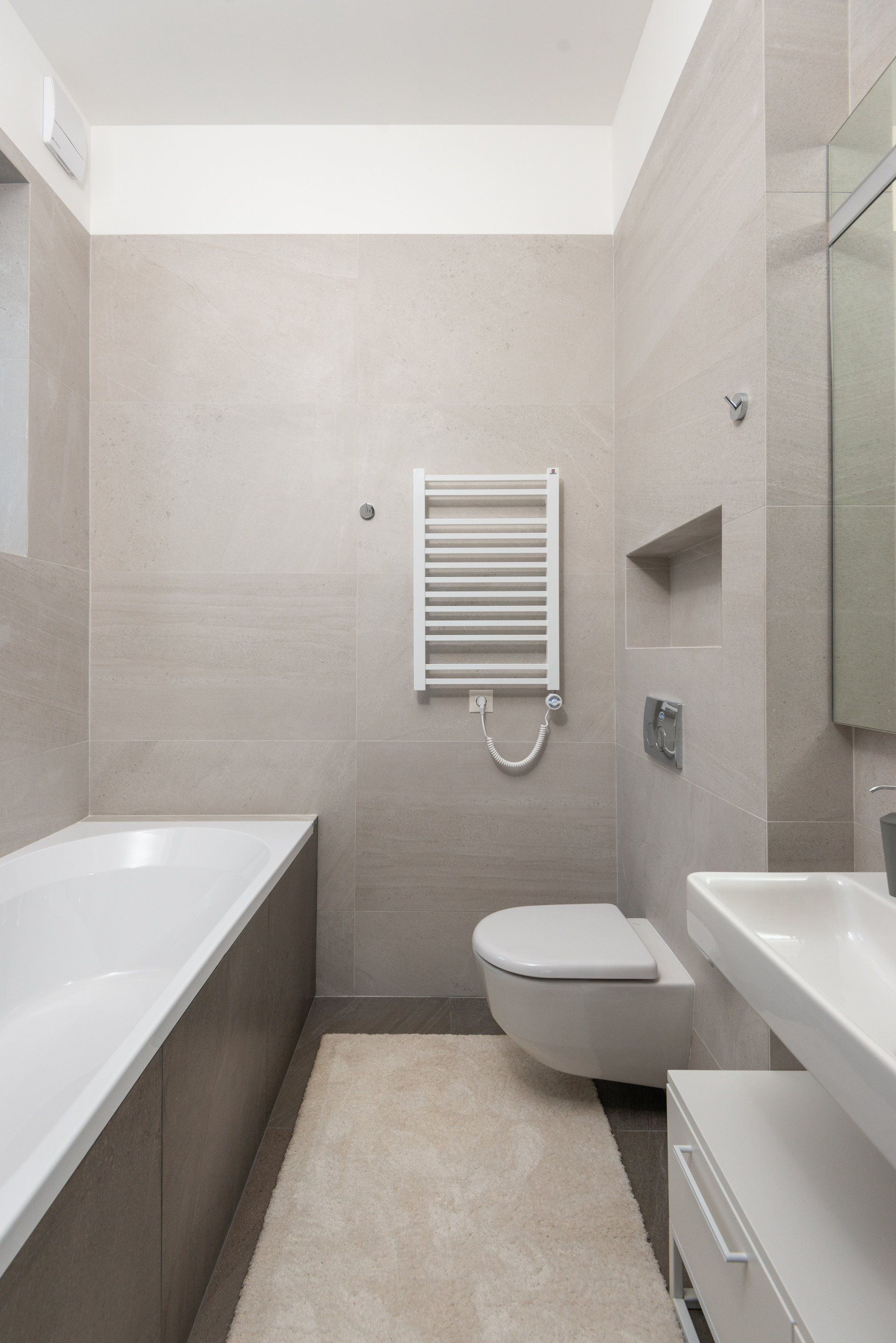 Modern bathroom with a bathtub, toilet, and sink; neutral gray tones.