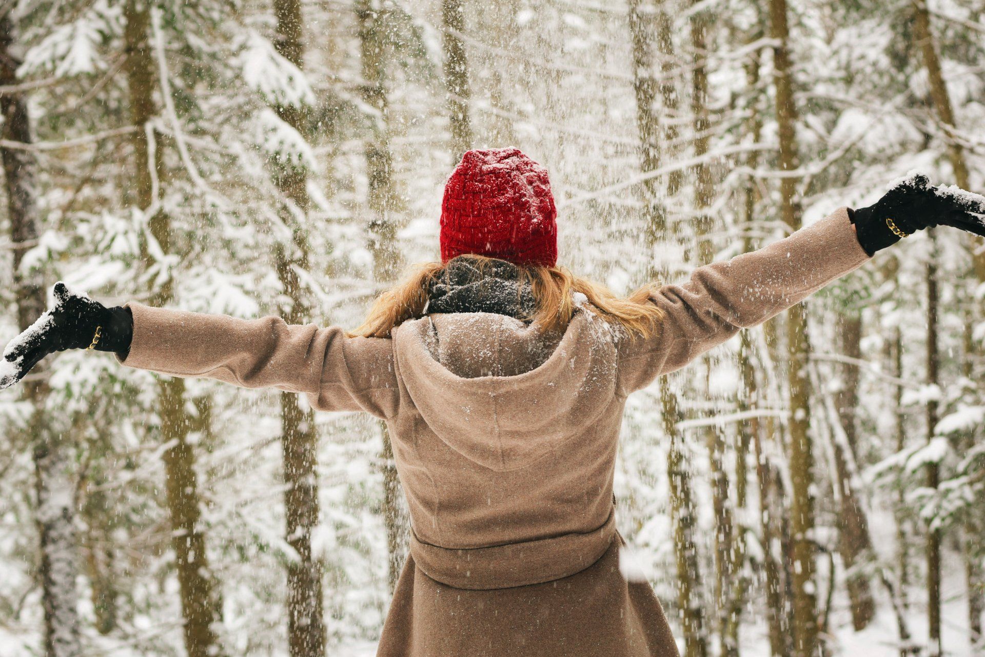 Eine Frau mit rotem Hut und Mantel steht mit ausgestreckten Armen im Schnee.