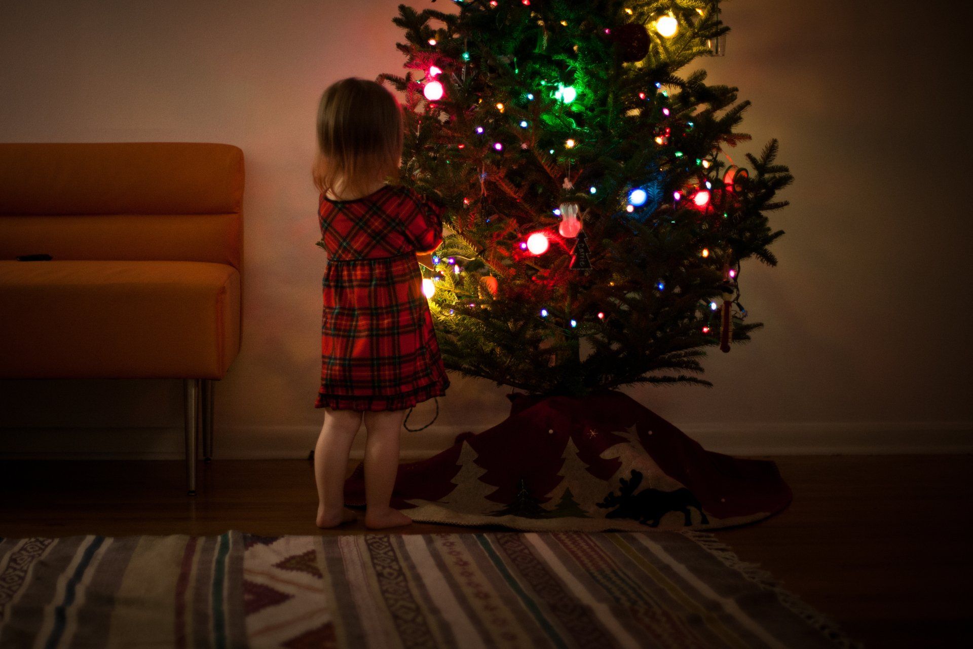 A little girl is decorating a christmas tree in a living room.