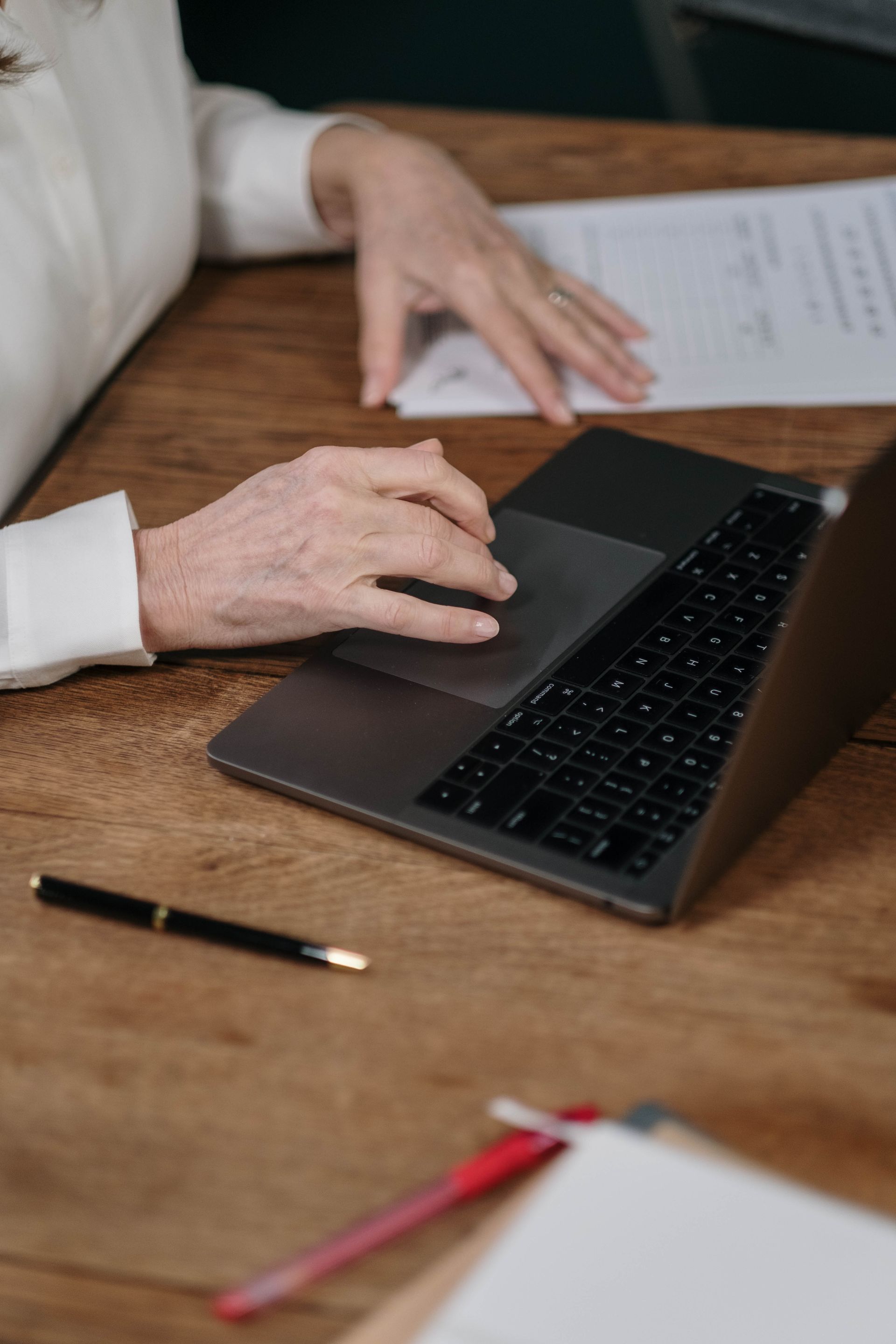 Uma pessoa está digitando em um laptop sobre uma mesa de madeira.