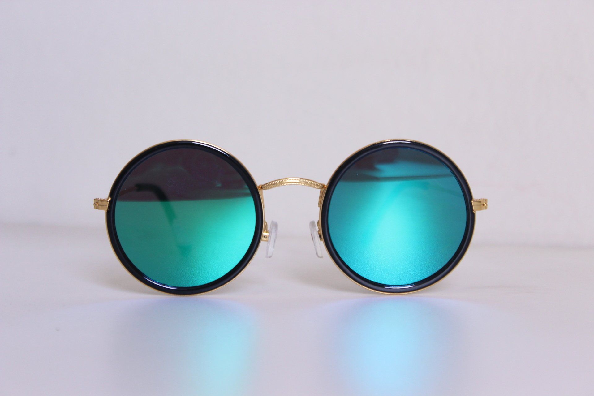 A pair of round sunglasses with green lenses on a white surface.