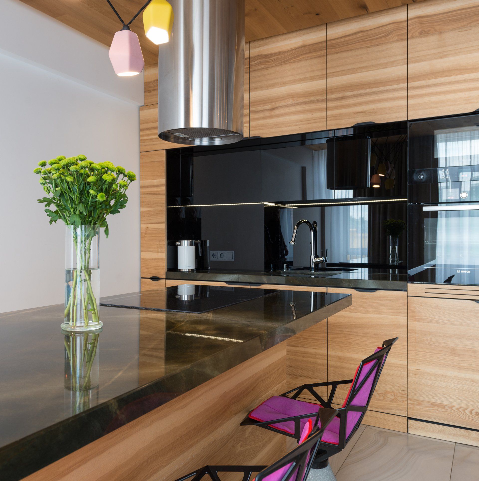 Modern kitchen with black glass cabinets, wood finishes, a dark island, and a pink chair