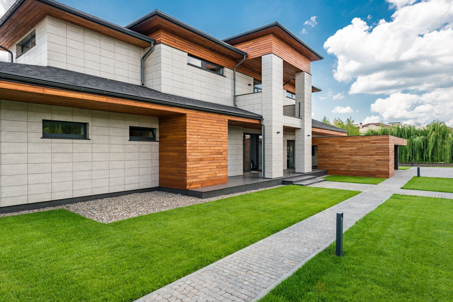 Modern two-story house with gray stone, wood accents, and a green lawn with a walkway