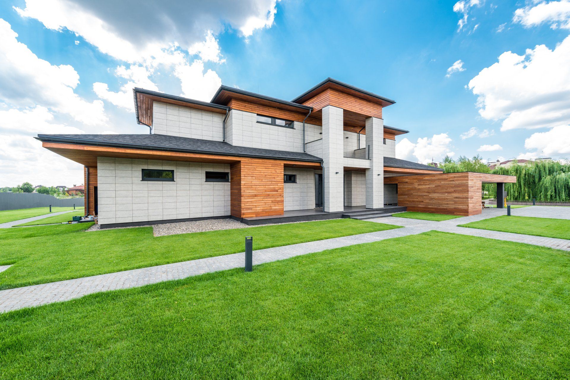 Modern two-story house with green lawn, wooden accents, and blue sky with clouds.
