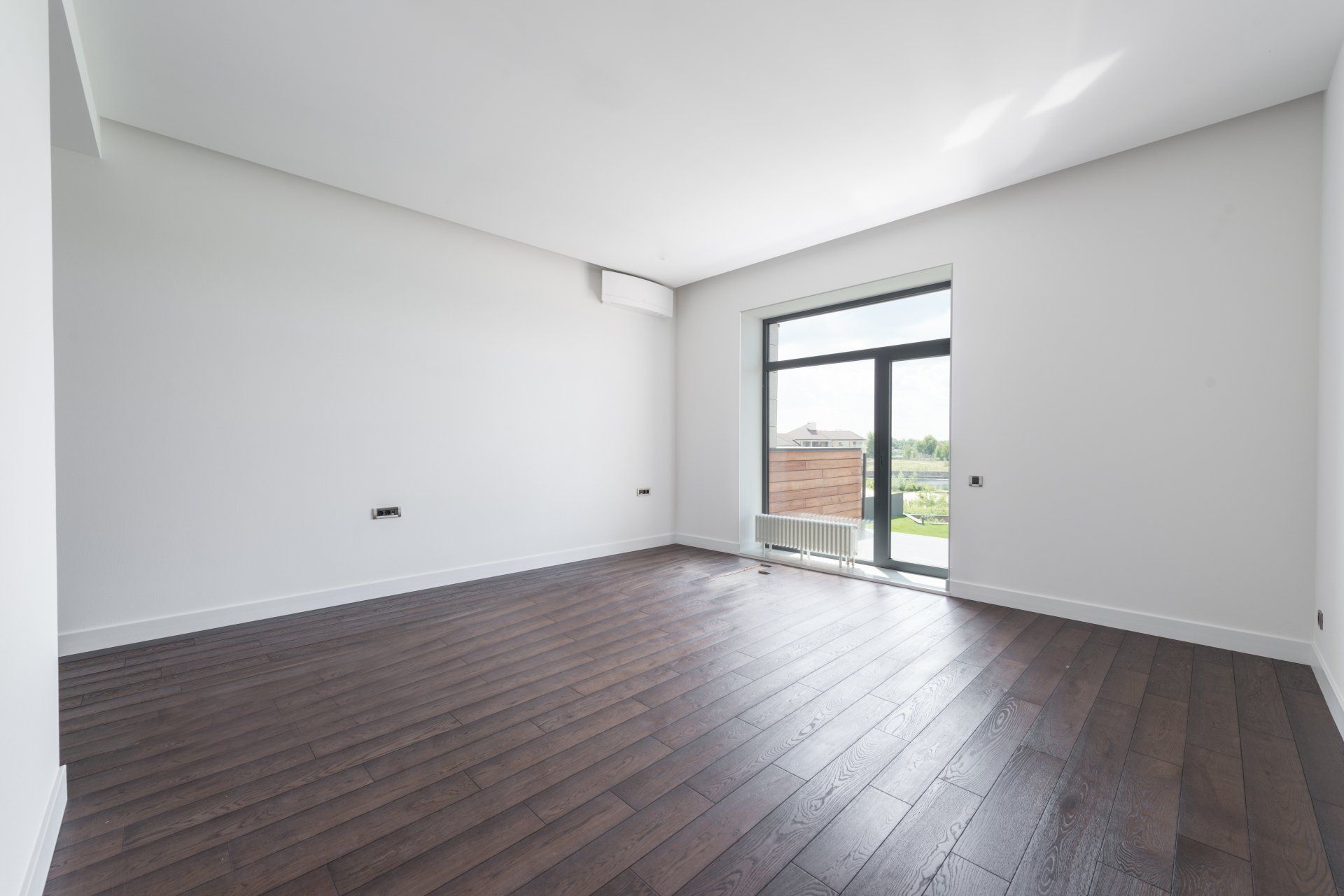 Empty modern room with dark wood floors, white walls, and a glass door to a balcony.