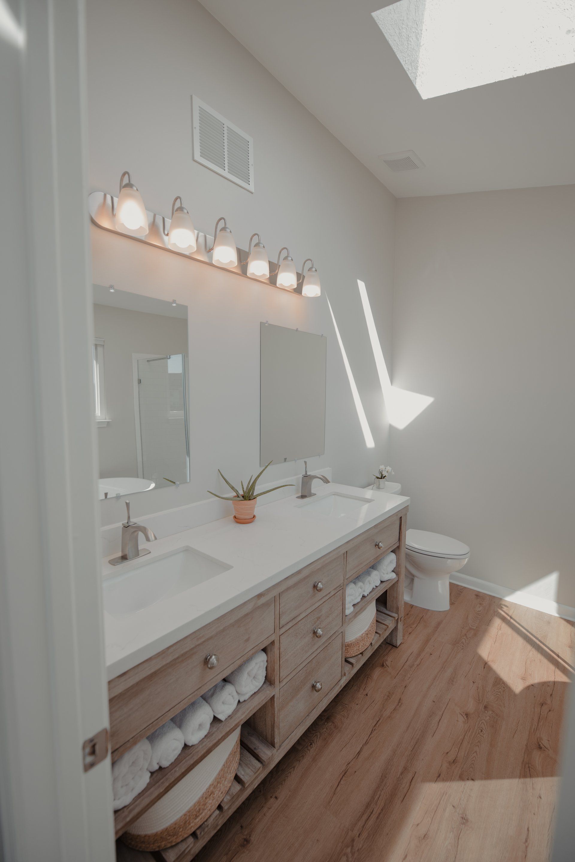A bathroom with two sinks , a toilet , and a skylight.