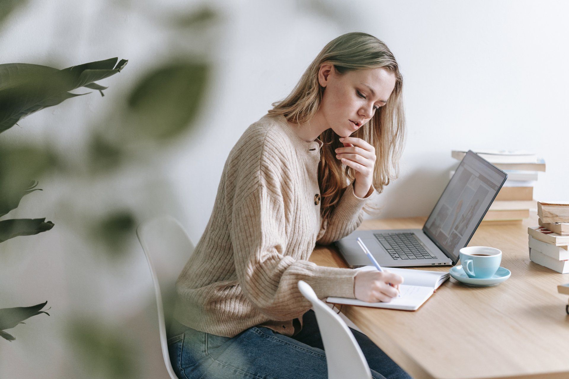 A woman is sitting at a desk with a laptop and a cup of coffee.