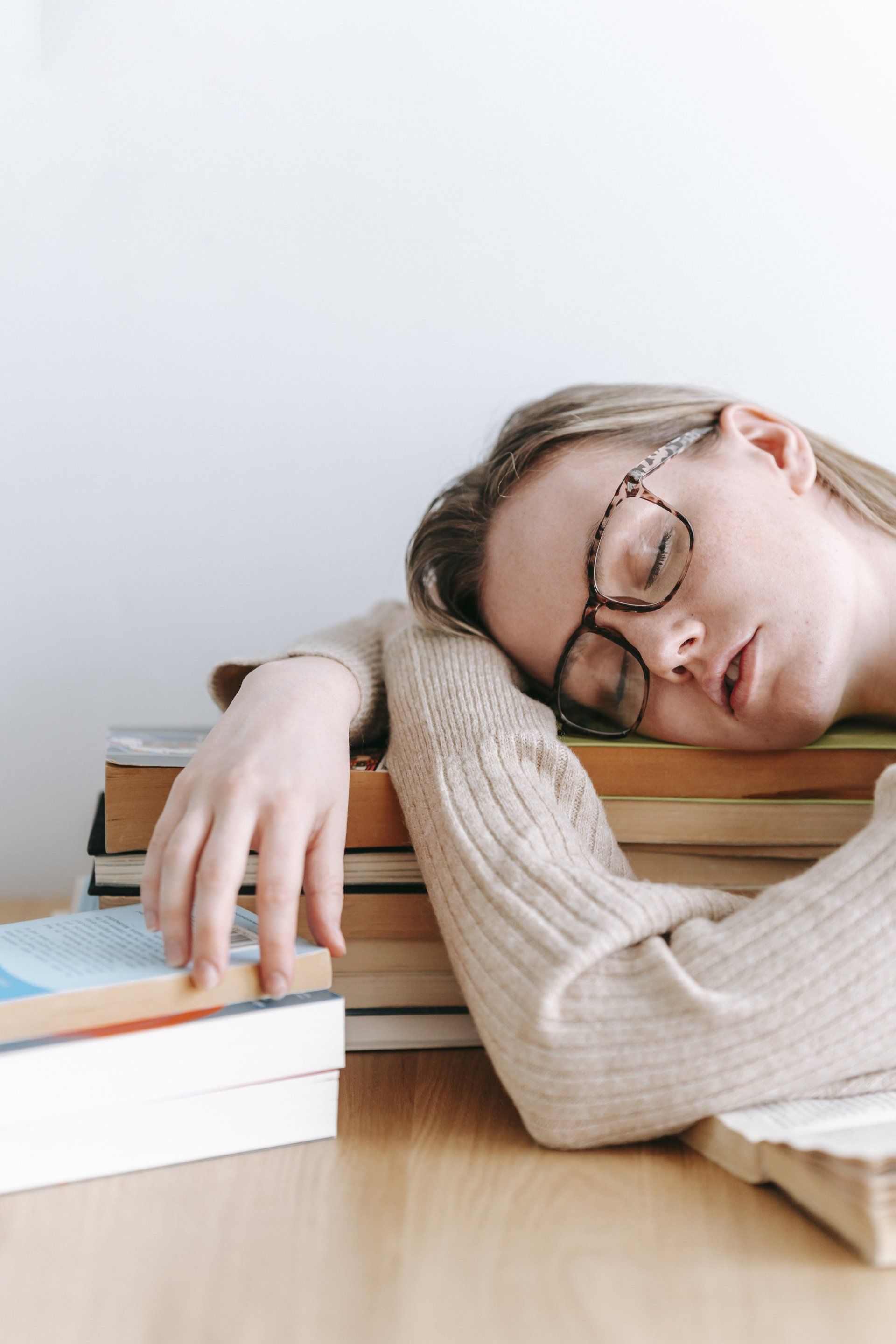 A woman wearing glasses is sleeping on a stack of books.