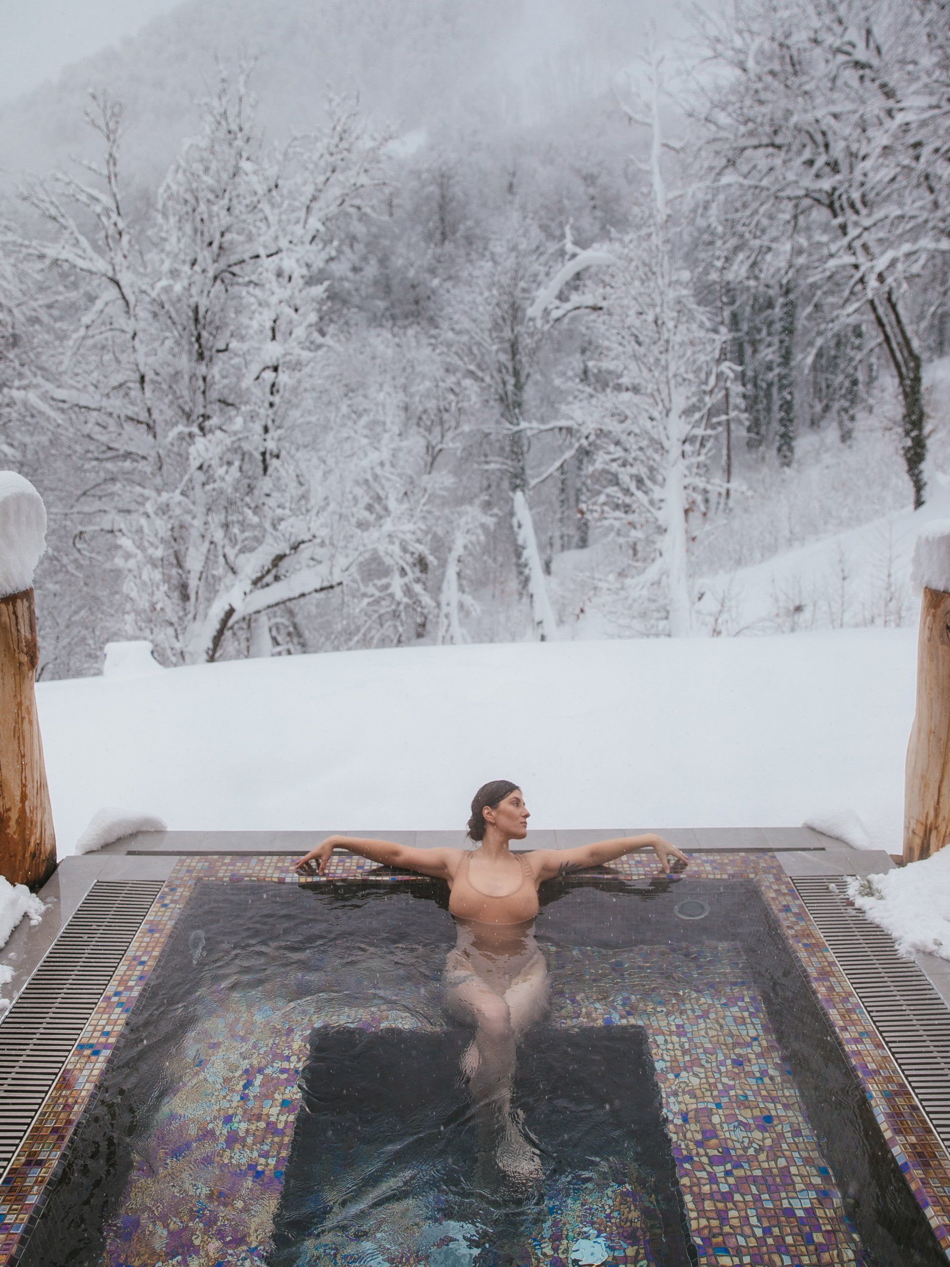 Une femme prend un bain dans un jacuzzi sous la neige.