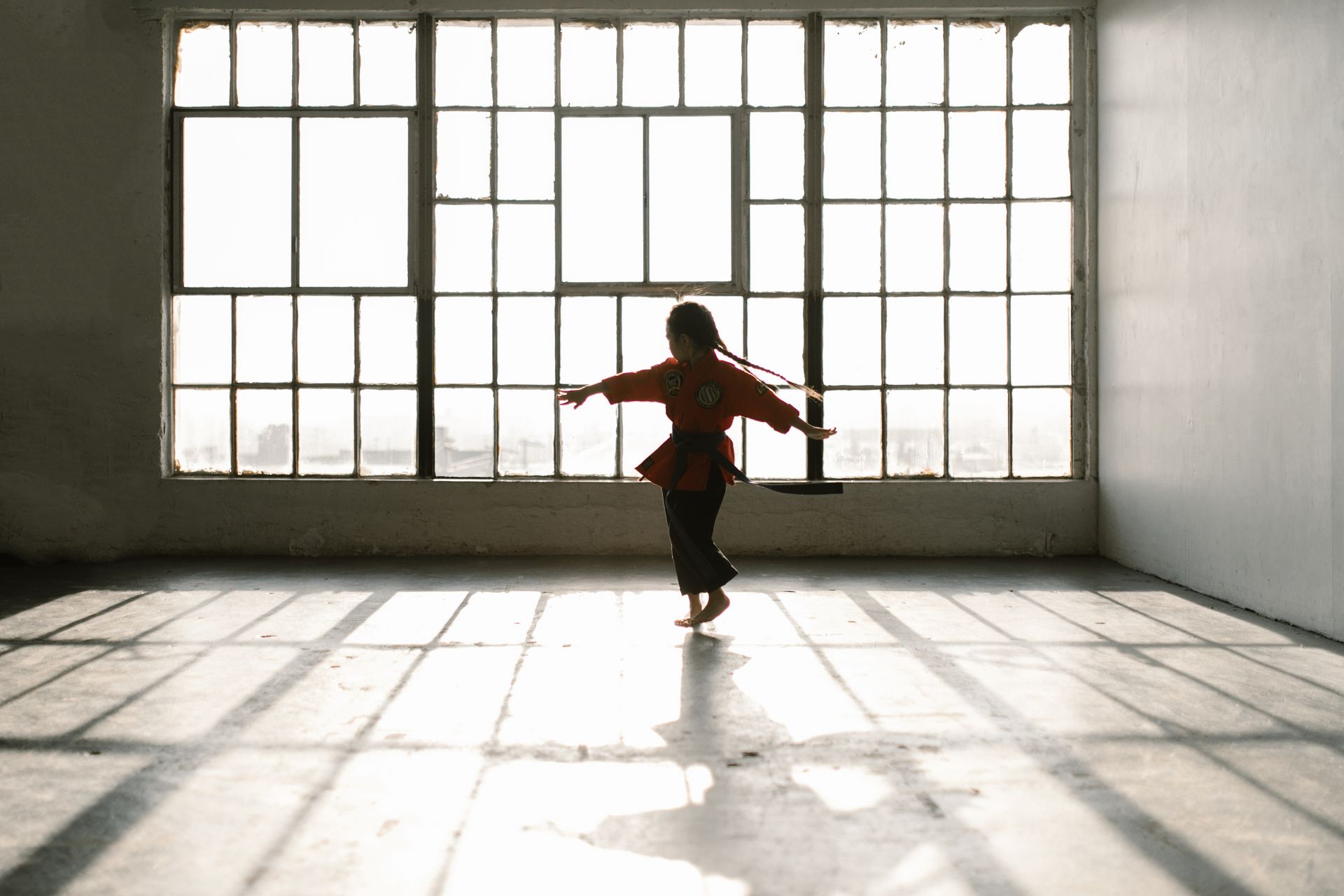 A little girl is dancing in front of a large window