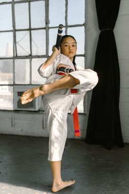 A young girl is practicing karate in a gym while holding a stick.
