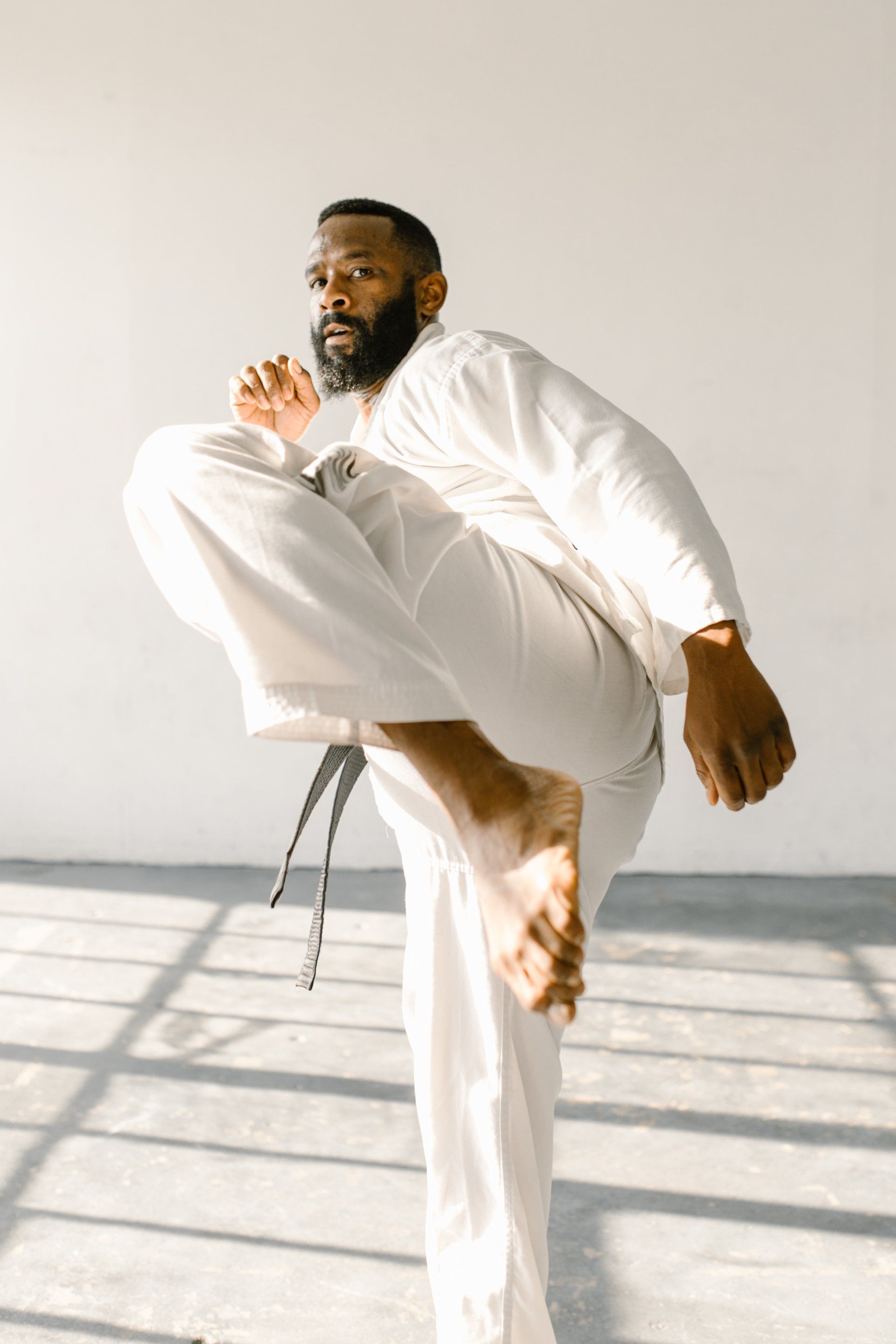 Een man in een wit karate-uniform schopt in de lucht.ieman