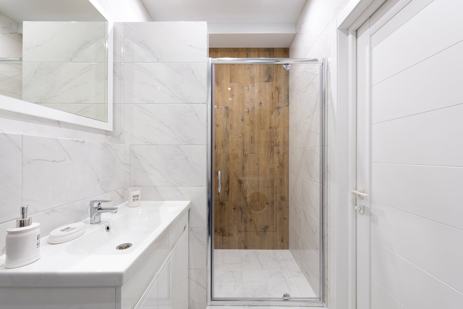 A bathroom with a sink , mirror and walk in shower with a custom shower door.