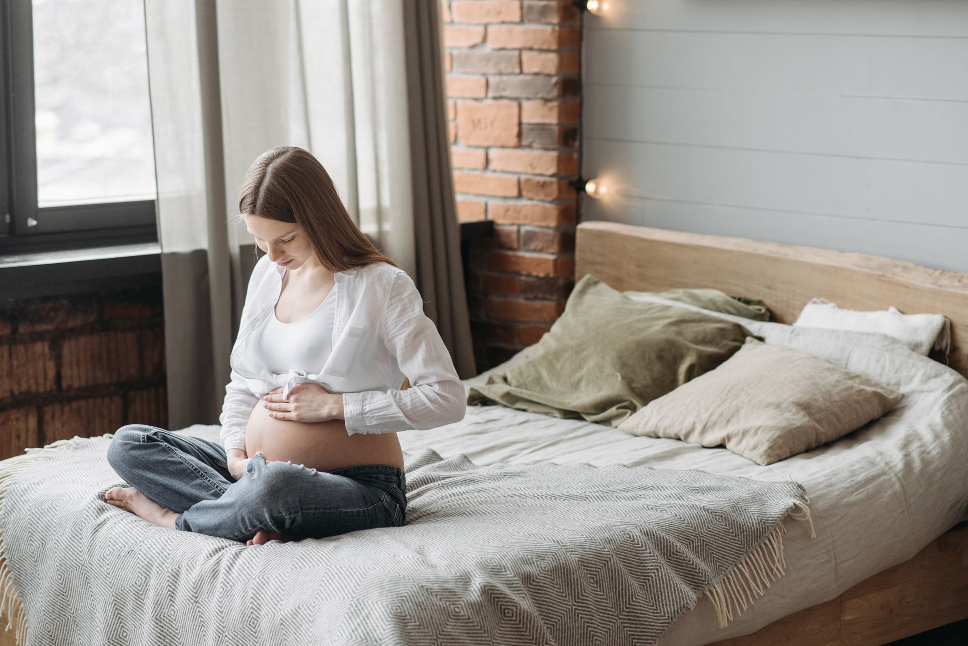 A pregnant woman is sitting on a bed holding her belly.