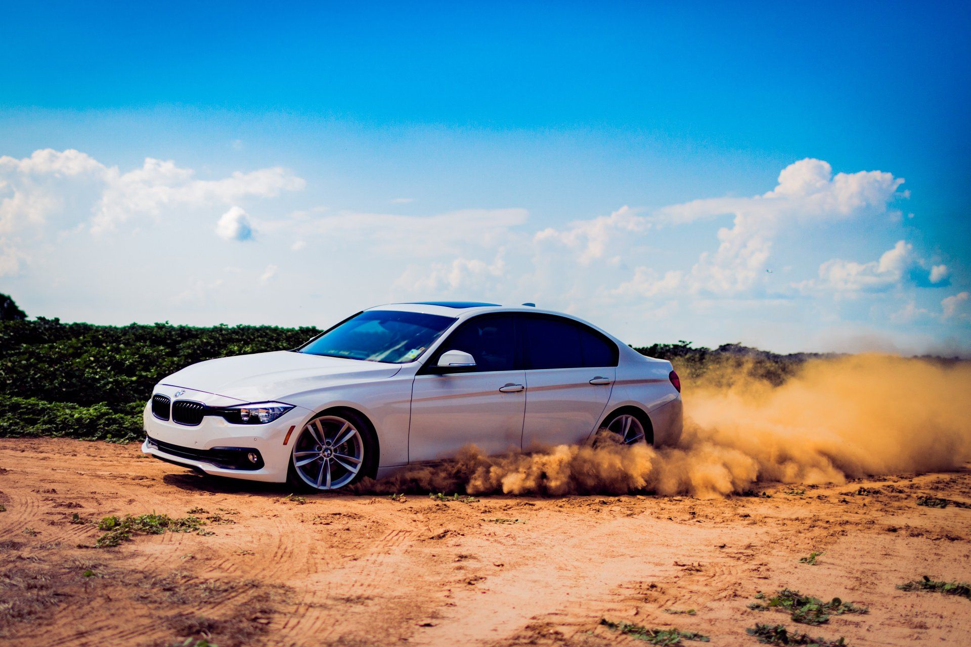 A white car is driving through the dirt on a dirt road.