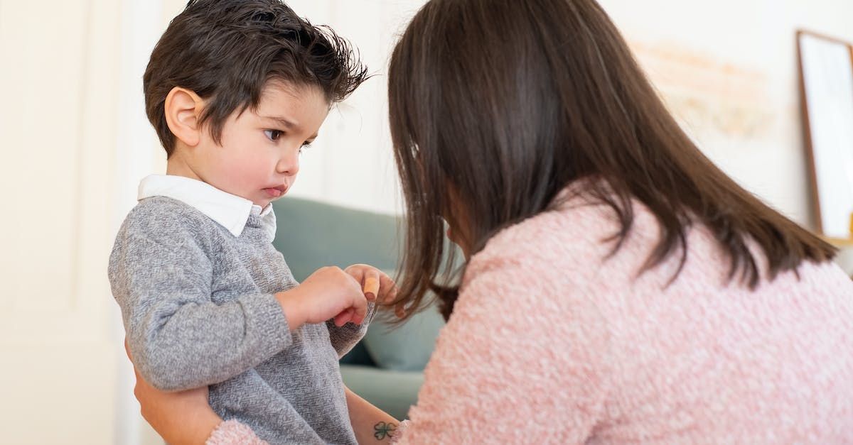 A woman is helping a young boy put on a sweater.