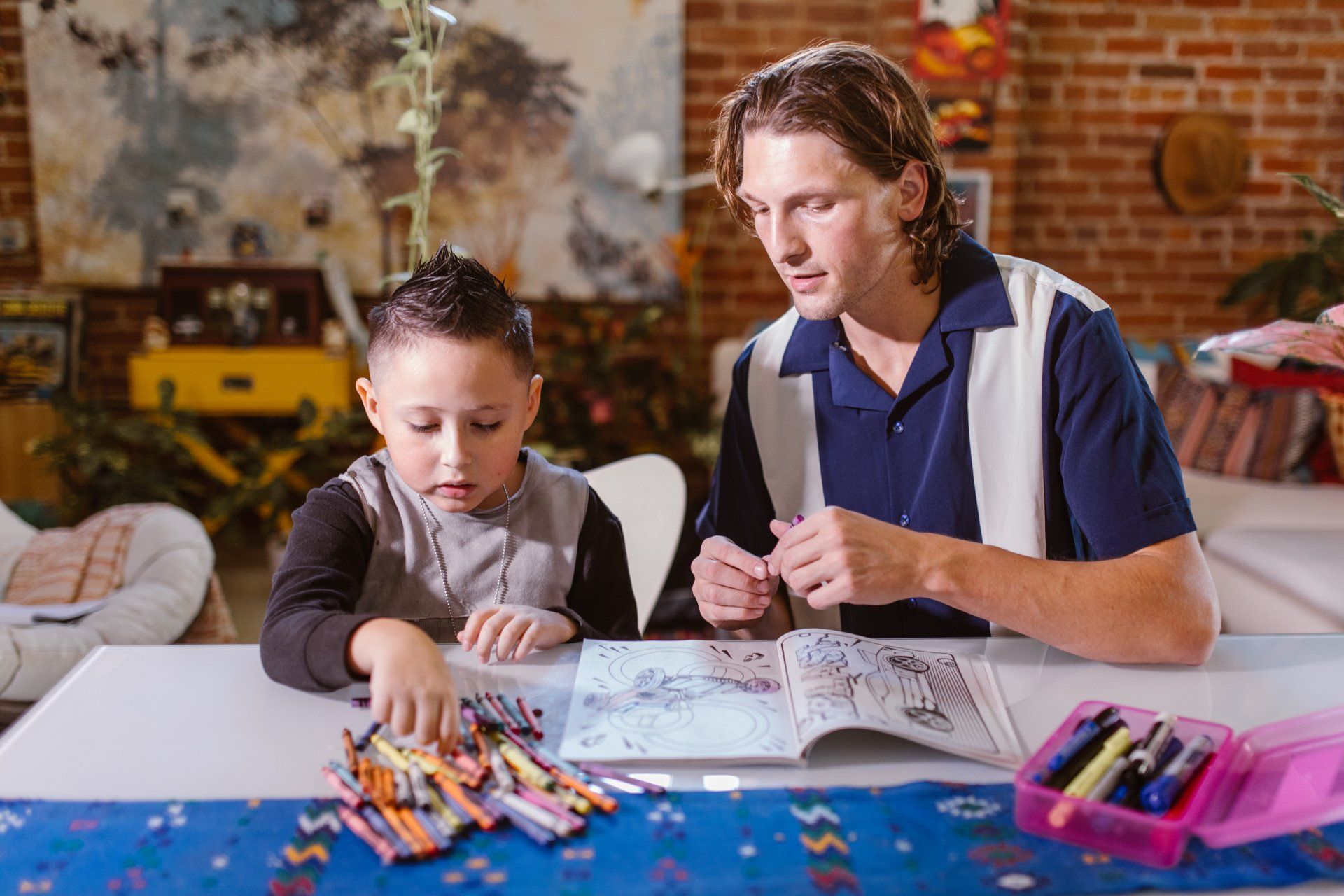 A man and a boy are sitting at a table drawing with crayons.