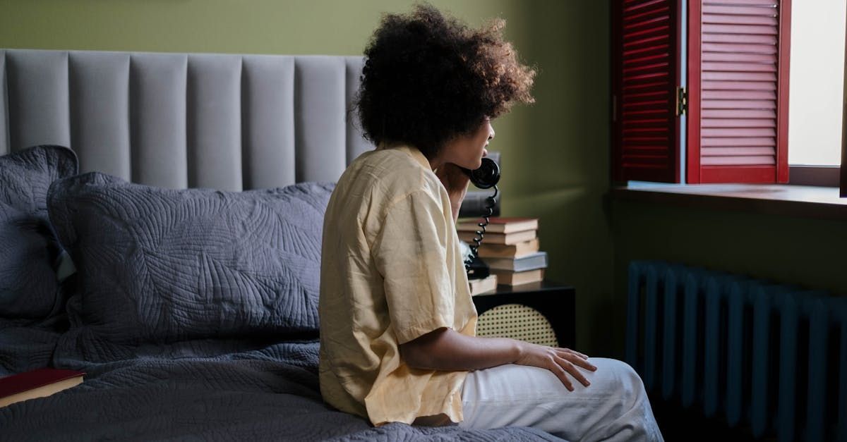 A woman is sitting on a bed talking on a cell phone.
