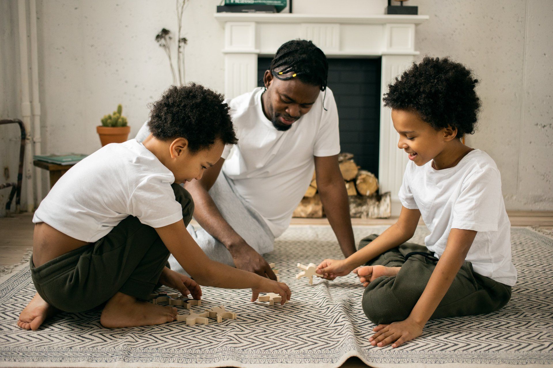 Father and two children playing game on patterned rug by fireplace.