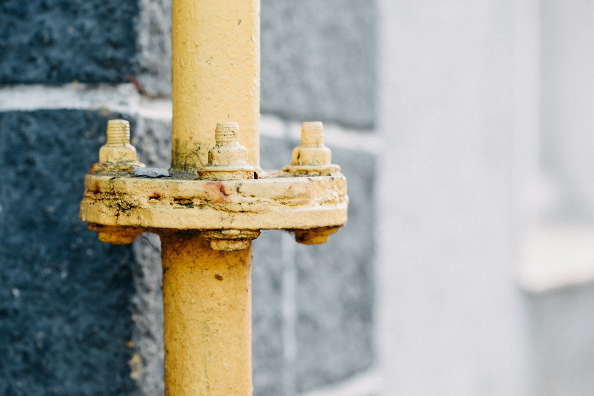 Close-up of a yellow metal pipe with a rusted flange against a gray concrete wall