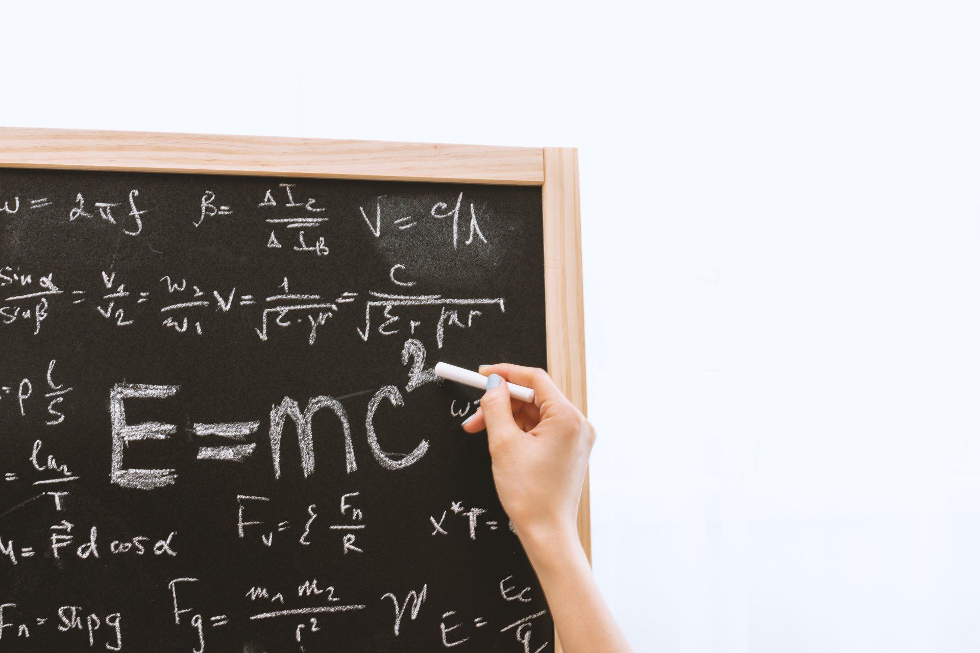 Handwriting on a chalkboard with physics equations, including E=mc², as a hand points with chalk.