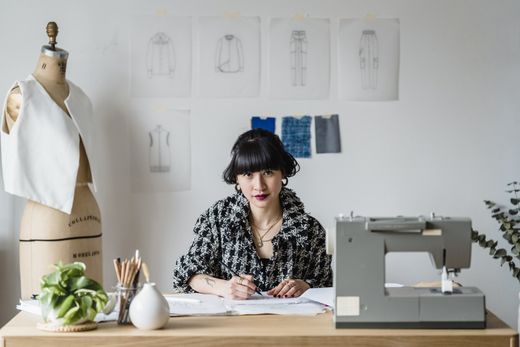 A woman is sitting at a desk in front of a sewing machine.