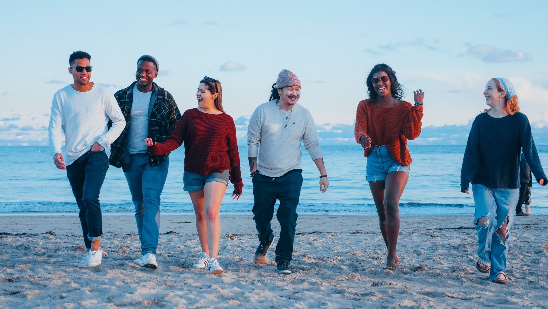 A group of diverse people on the beach laughing and walking