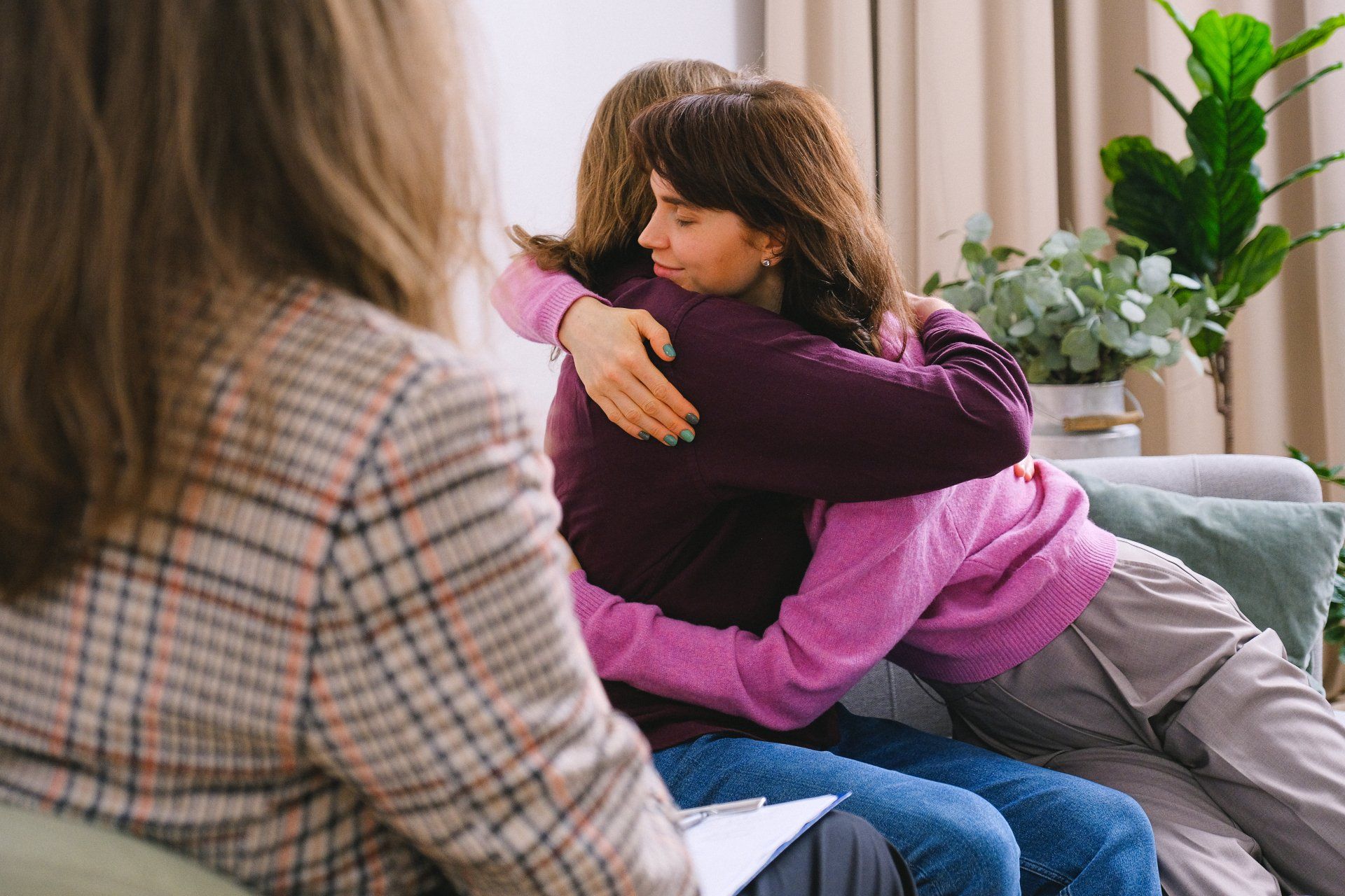Two women are hugging each other while sitting on a couch.