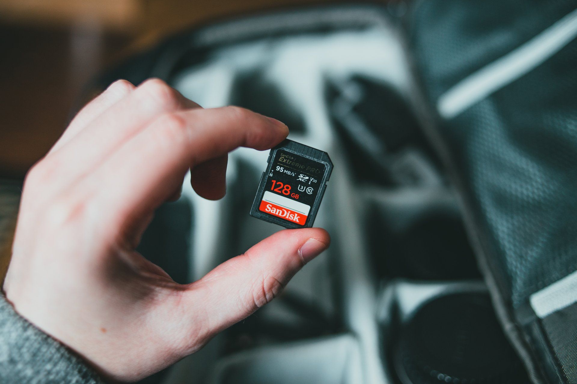 A person is holding a sd card in their hand in front of a camera bag.
