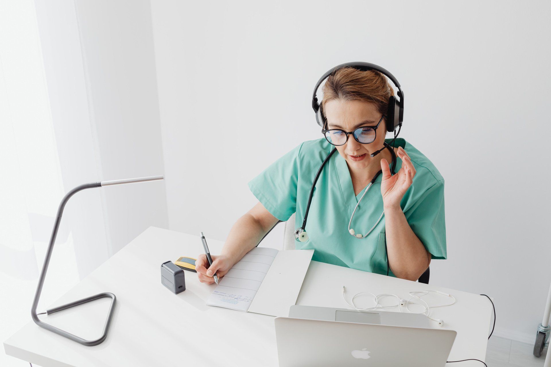A nurse wearing headphones is sitting at a desk in front of a laptop computer.