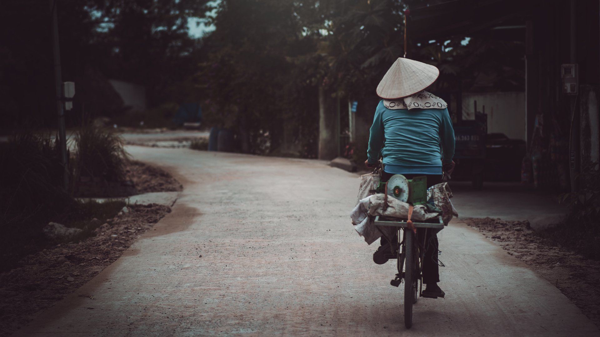 A woman wearing a conical hat is riding a bicycle down a road.