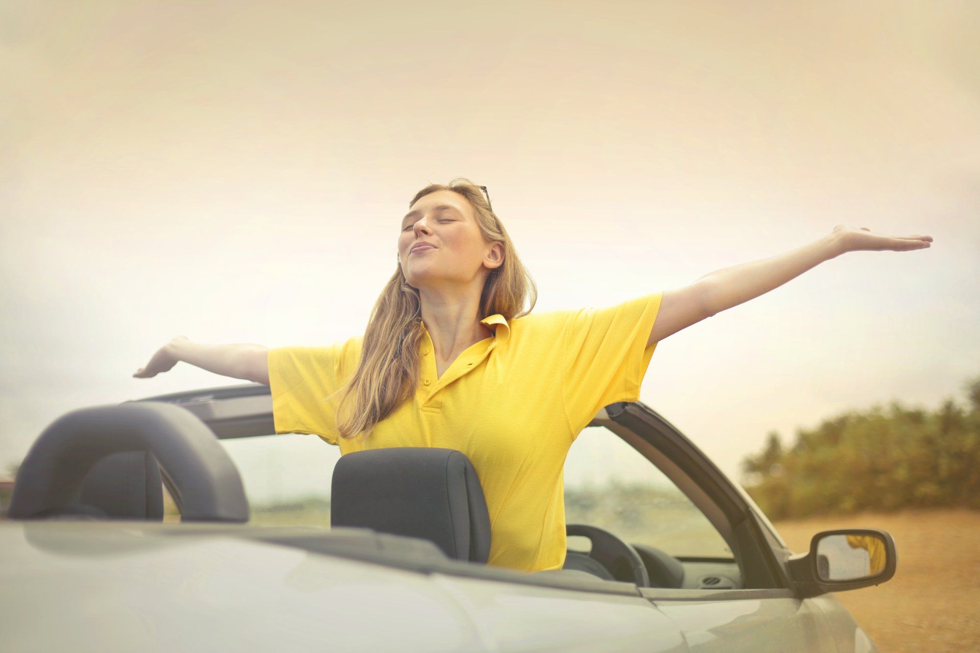 a woman in a yellow shirt is sitting in a convertible car with her arms outstretched .
