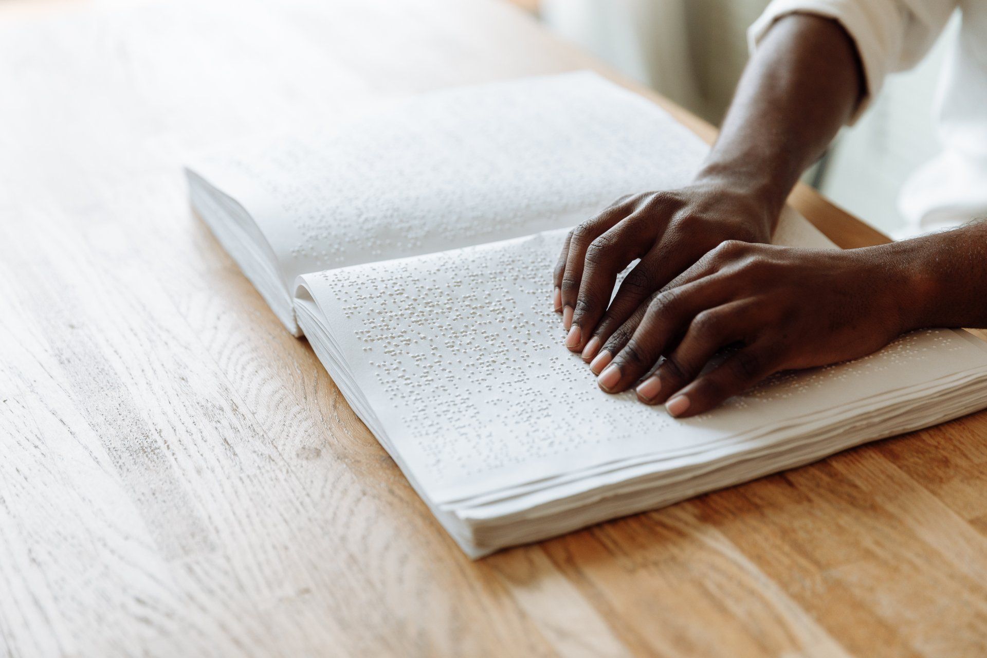 une personne lit un livre en braille sur une table en bois.