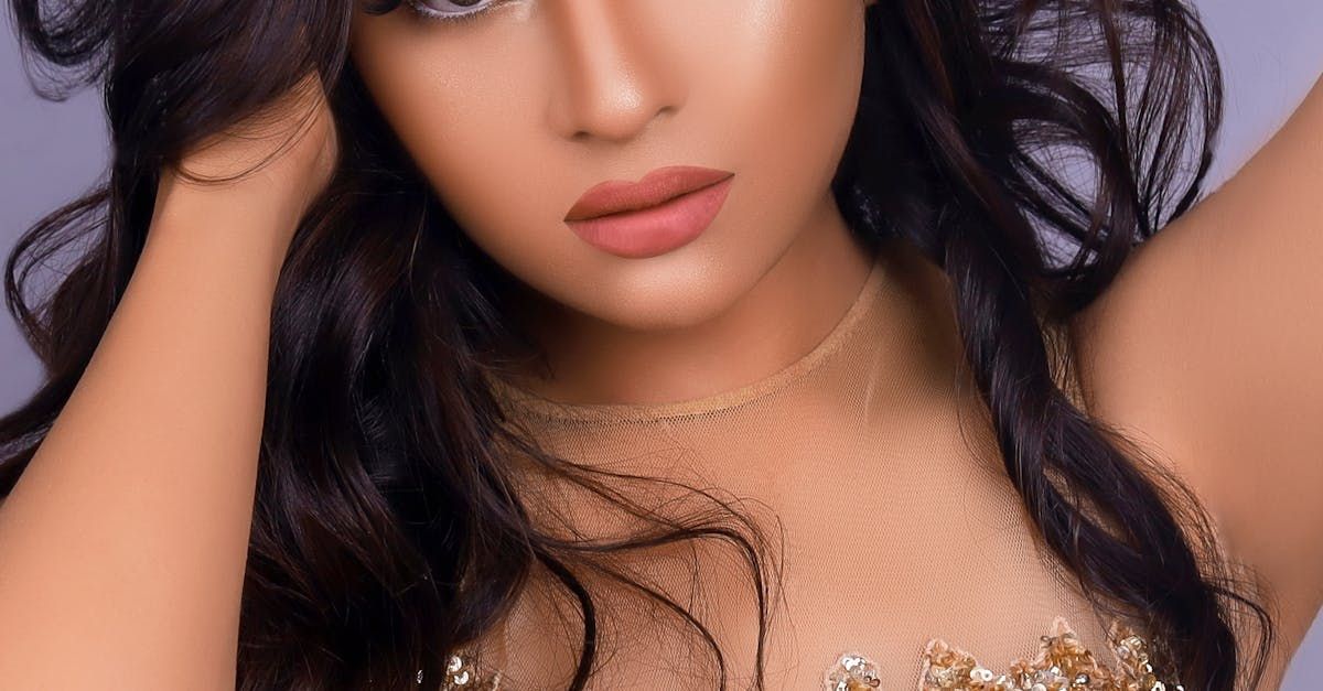 Woman with dark wavy hair, wearing a gold-toned dress, looking at the camera.