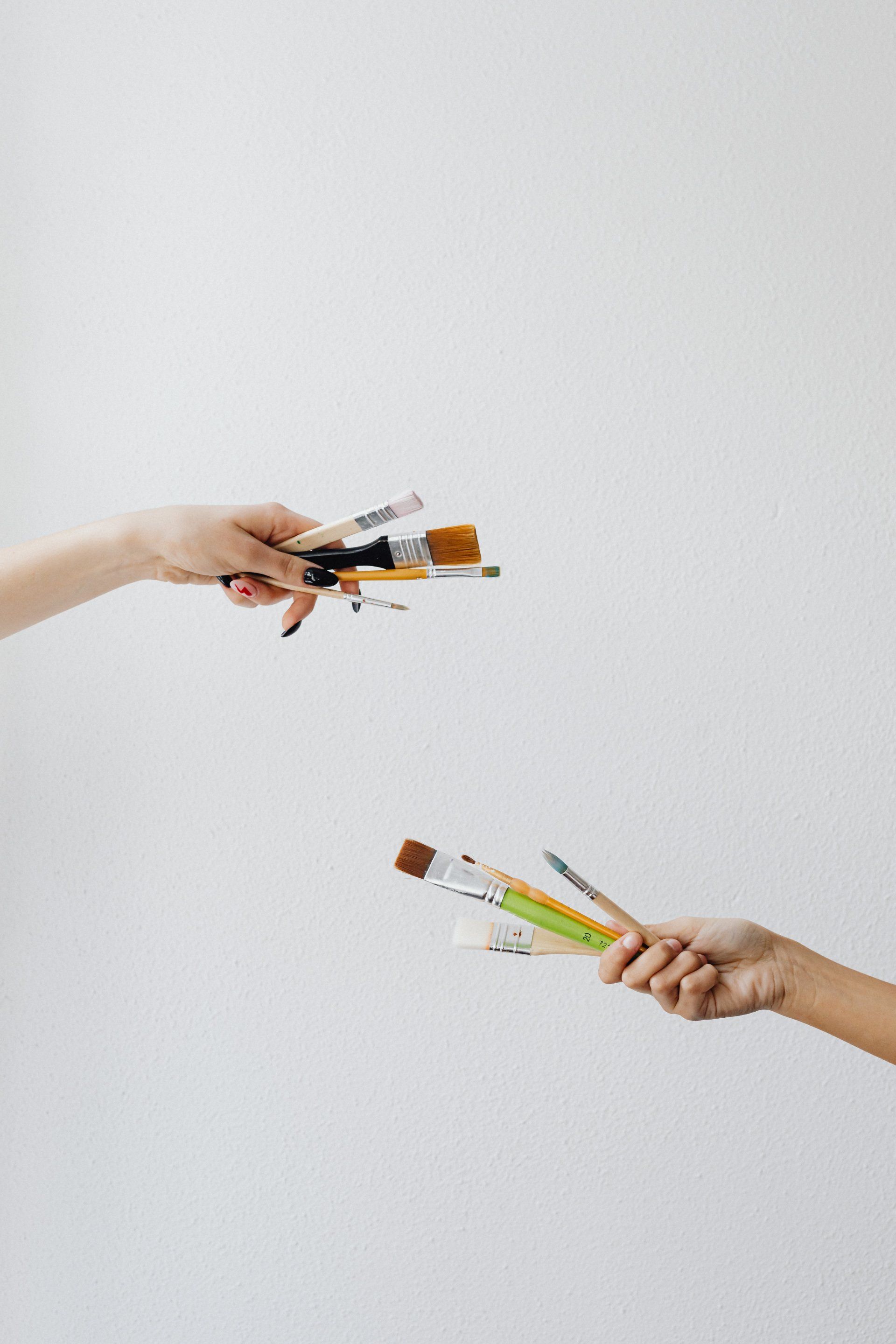 Two people are holding paint brushes in their hands.