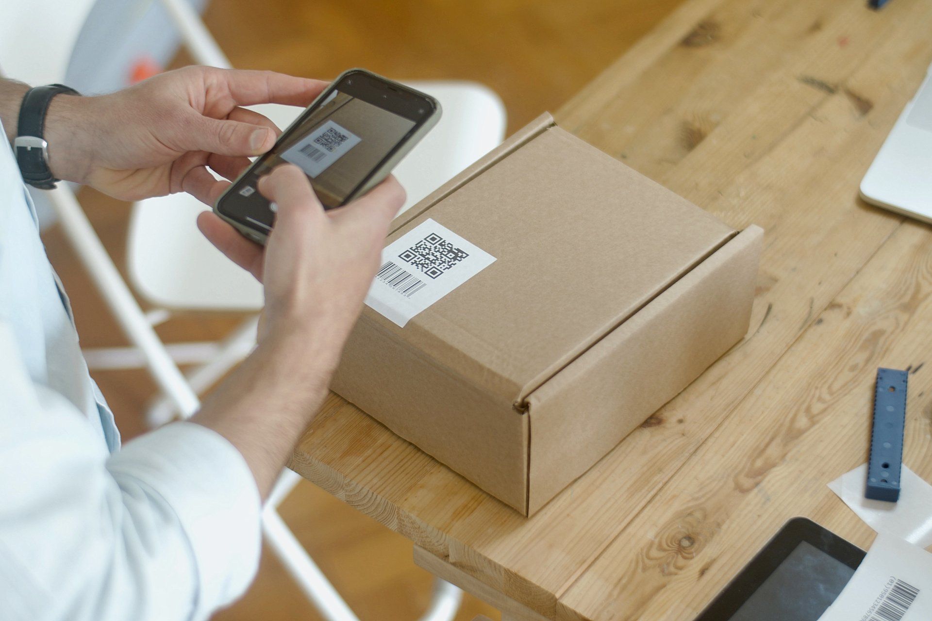 A man is using a cell phone to scan a barcode on a cardboard box.