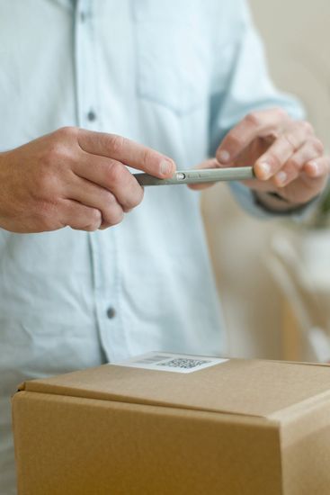 A man is holding a cell phone in front of a cardboard box.