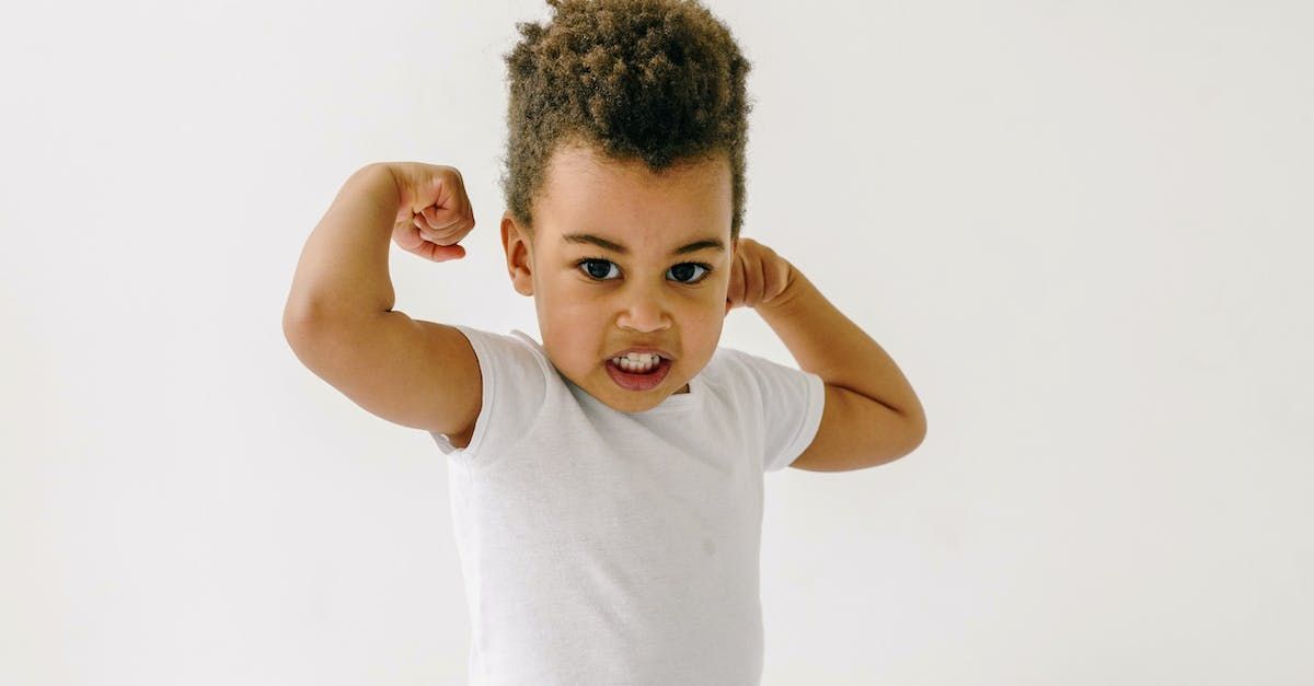 A young boy in a white shirt is flexing his muscles.