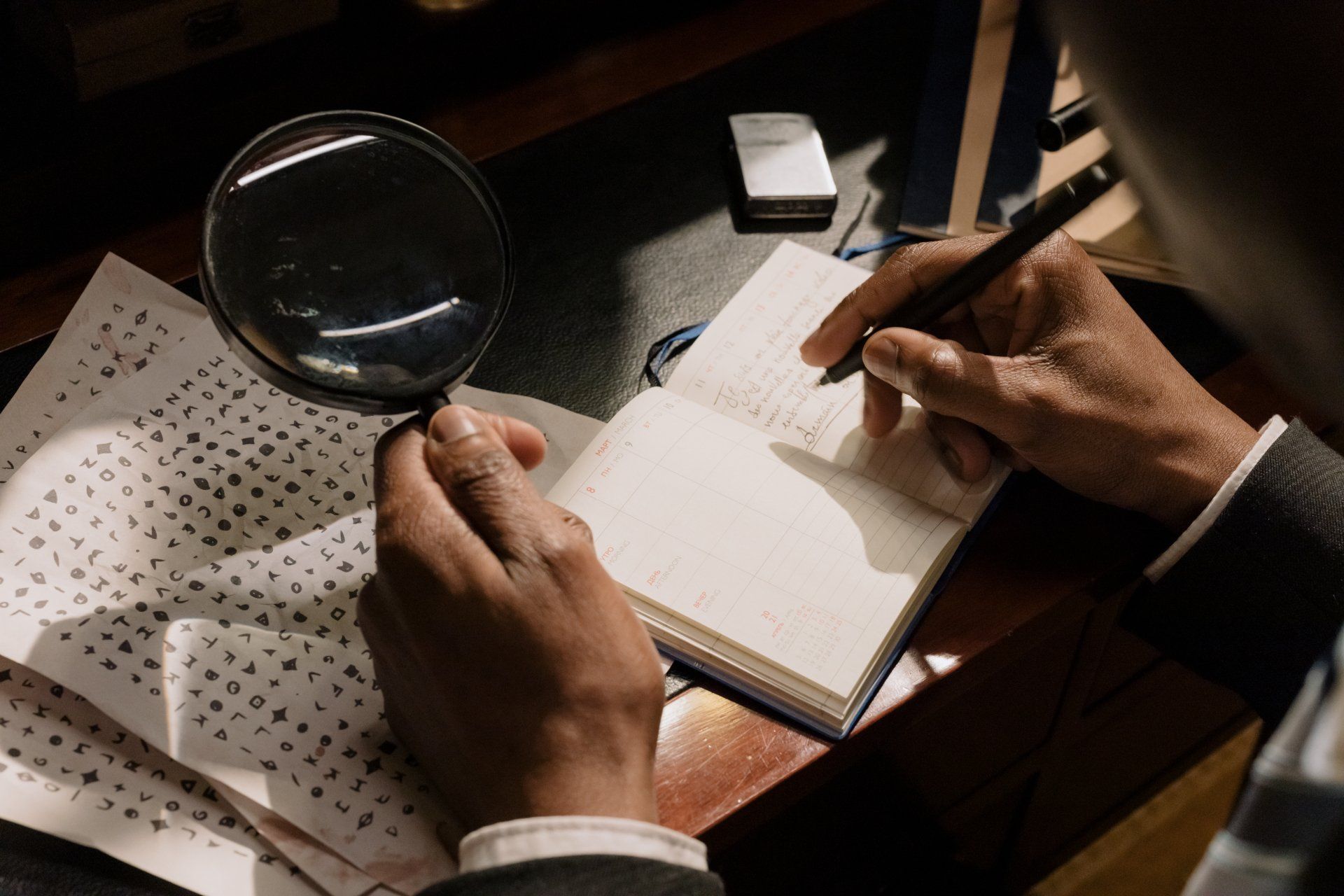 A man is holding a magnifying glass and writing in a notebook.