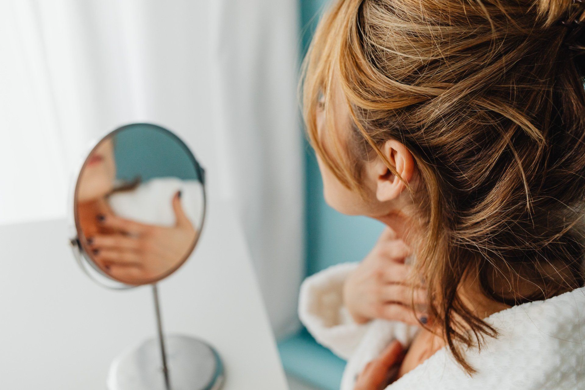 A woman is looking at her neck in a mirror.