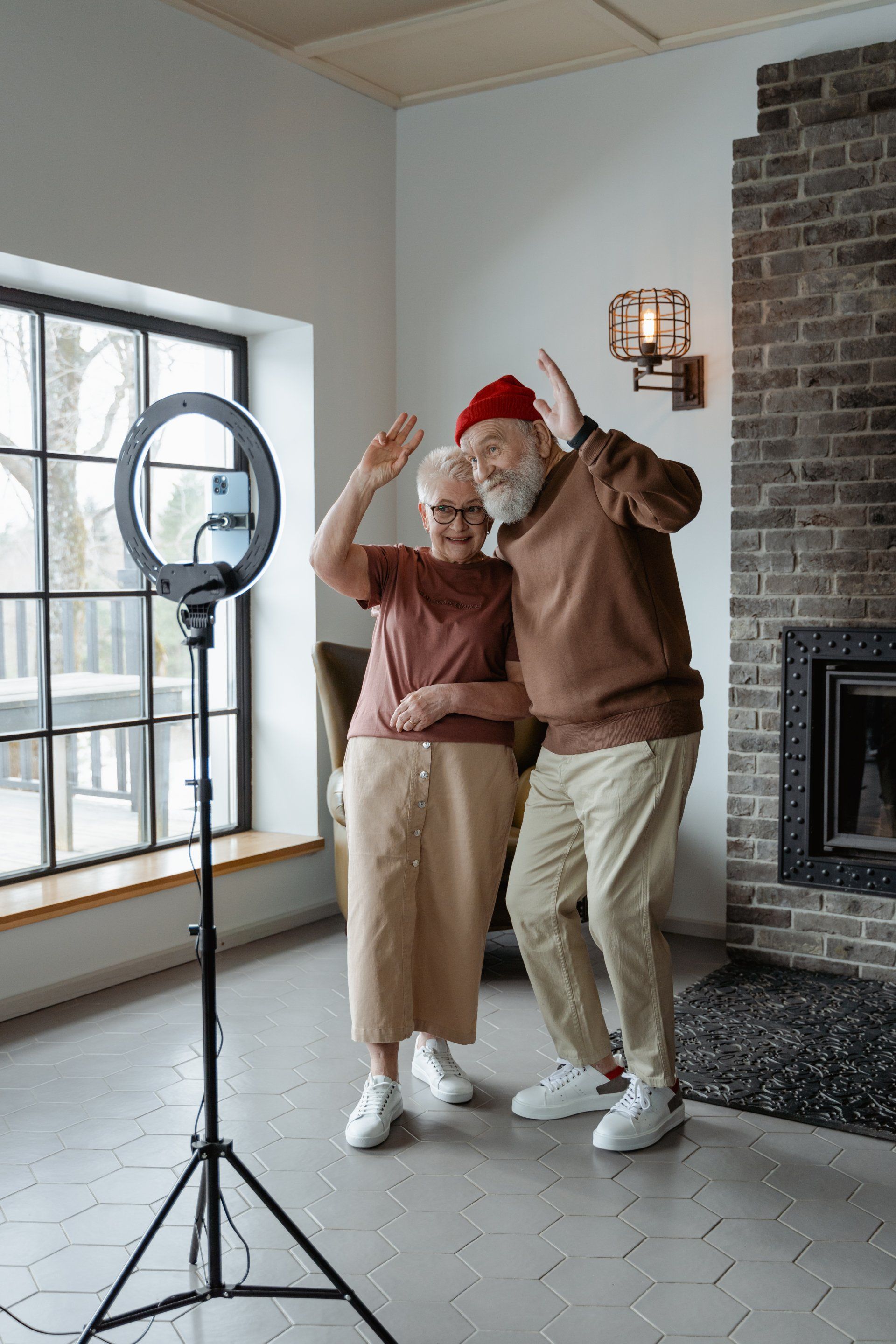 An elderly couple is dancing in front of a ring light in a living room.