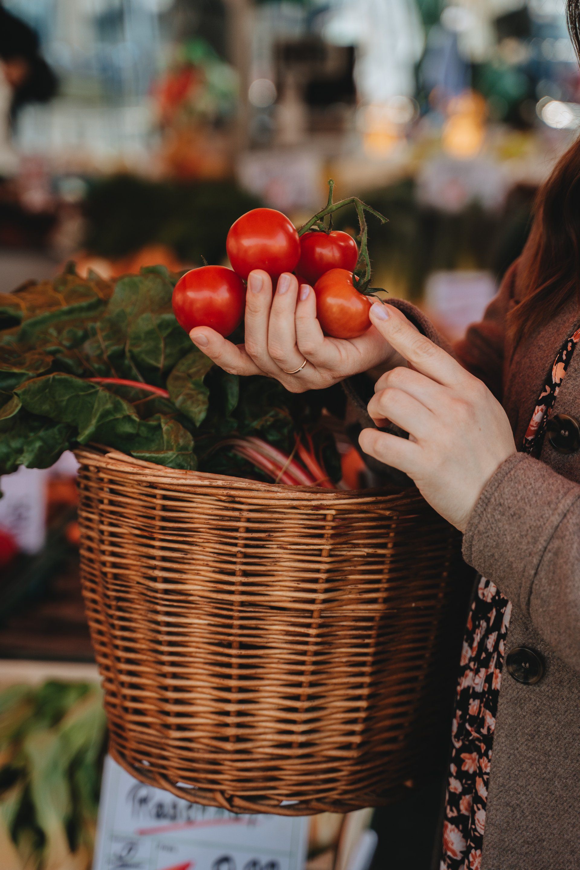 Hände halten rote Tomaten über einem Weidenkorb auf einem Freiluftmarkt.