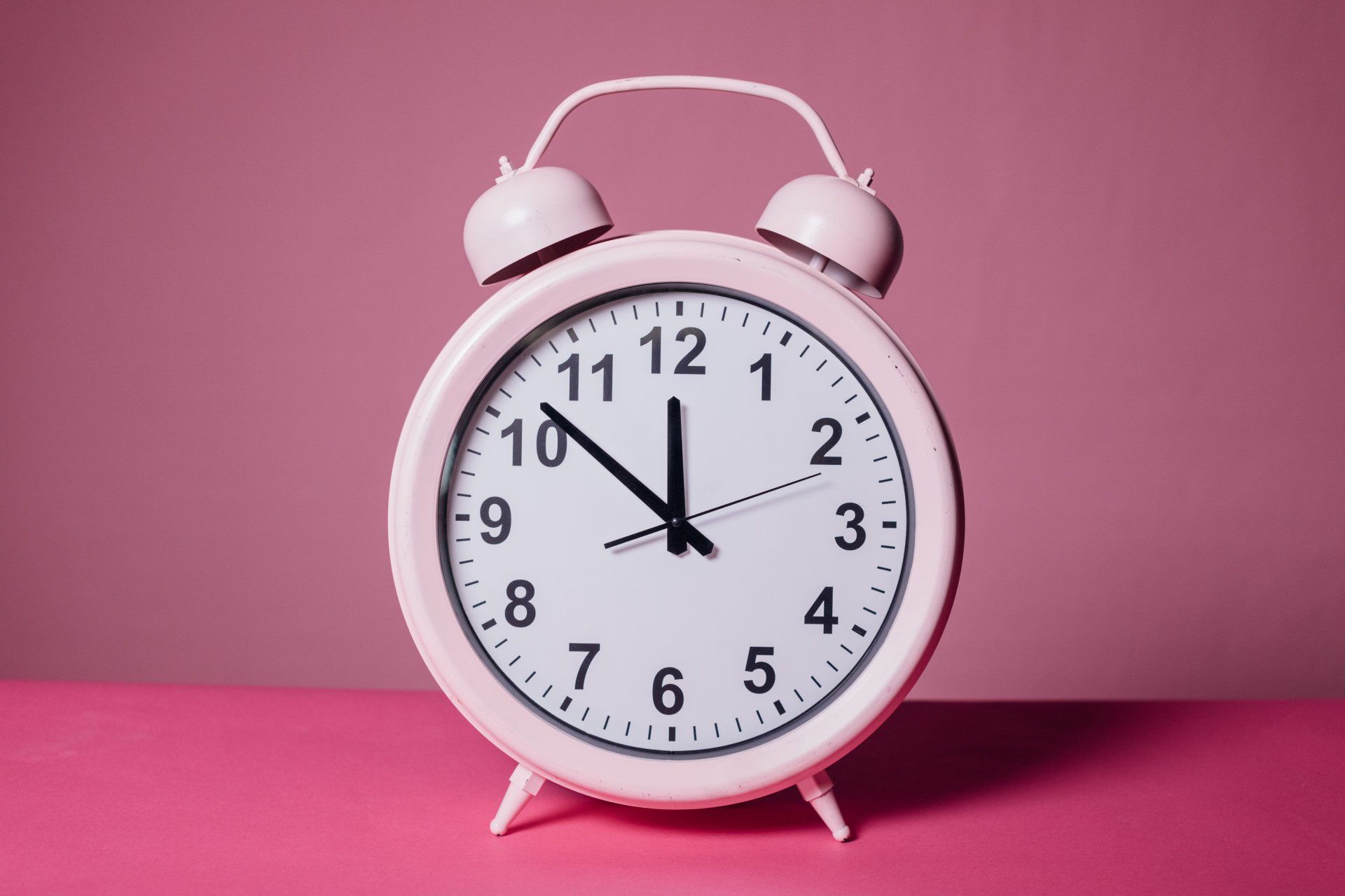 Pink alarm clock set to 11:00, with a pink background and surface.