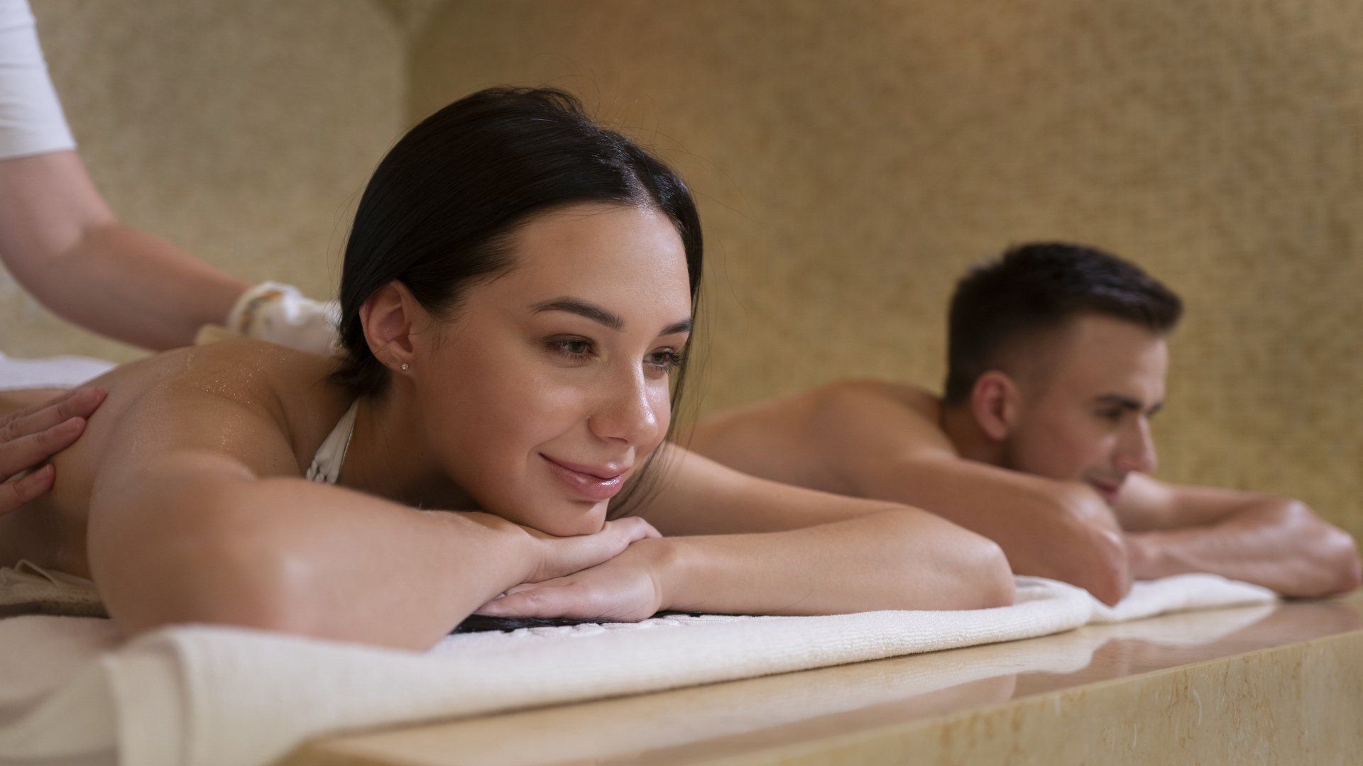 Two people resting on massage tables in a spa, smiling softly in a calm, warm room
